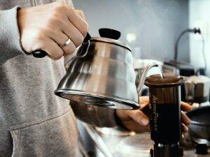a man pouring hot water from his kettle into a coffee maker, showing effective use of a kettle without limescale issues